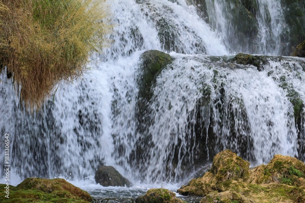 Obraz Editorial image of the Kravice Waterfall in Herzegovina, captured on August 24, 2025, showcasing cascading water over moss-covered rocks.
