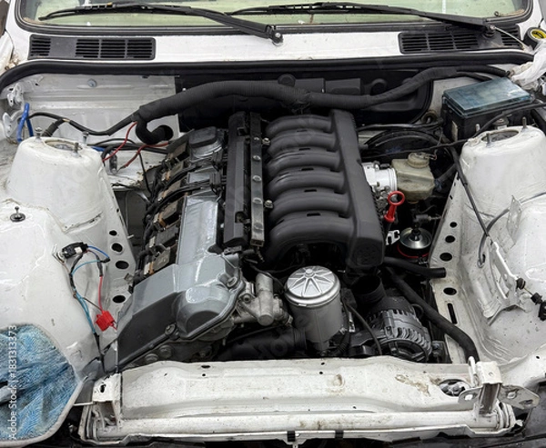 Obraz Mechanics work on upgrading a car's engine with new parts in a garage setting