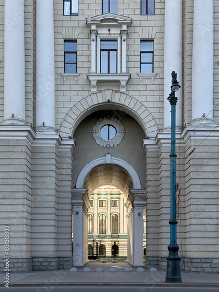 Obraz People walk through a large archway of historic architecture in a busy city center