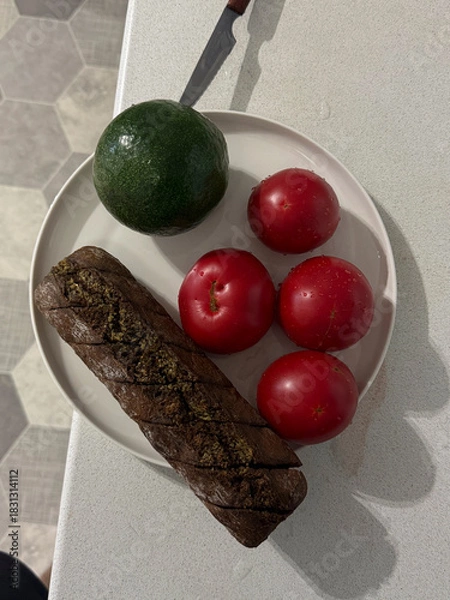 Obraz A plate holds a green avocado, red apples, and a rolled dish on a clean countertop