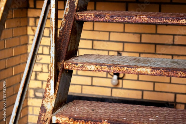 Obraz Old rusted metal staircase leaning against weathered brick structure with warm lighting