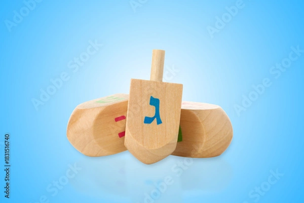 Fototapeta Three wooden dreidels with Hebrew letters resting against blue