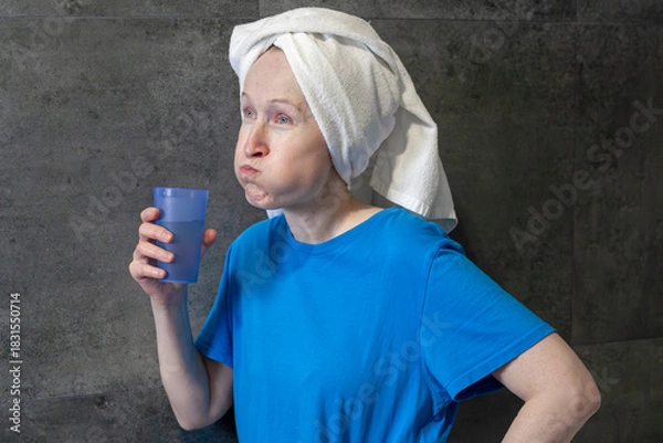 Obraz Woman rinsing mouth with water from a cup. Morning dental hygiene routine. Oral care and freshness concept for daily health.
