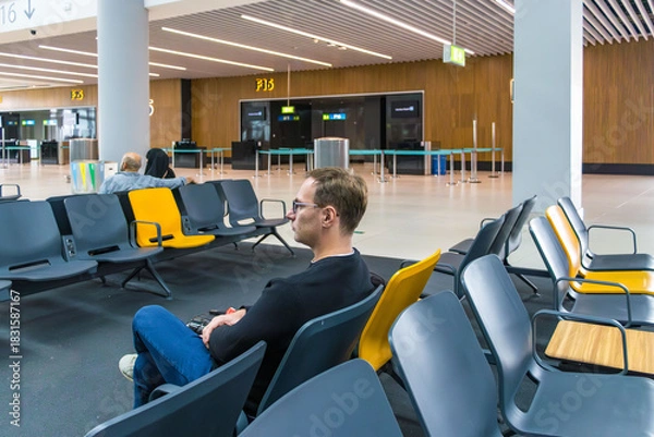 Fototapeta Man sitting in airport waiting area with luggage and backpack, waiting for flight, modern terminal interior