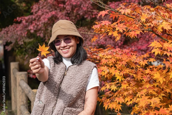 Obraz Woman holding autumn leaf outdoors near colorful fall foliage in park