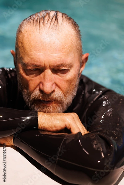 Fototapeta Senior swimmer in diving suit resting at poolside 