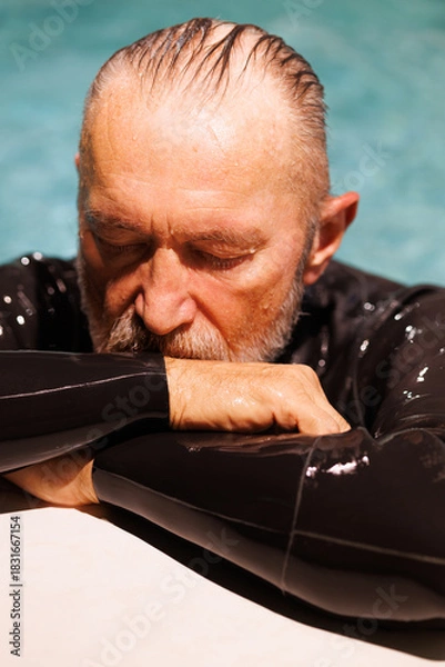 Fototapeta Portrait of grey haired free diver in wetsuit resting at poolside 