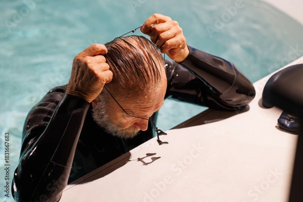 Fototapeta Grey haired diver in wetsuit wearing nose clip at poolside before training 