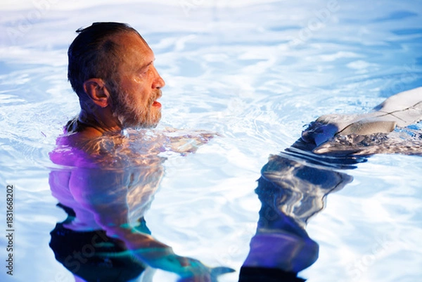 Fototapeta Side view of senior diver taking off wetsuit in swimming pool with light 