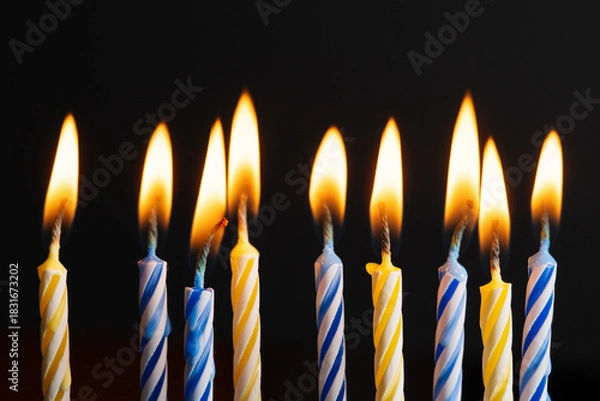Fototapeta Yellow and blue birthday candles burning with soft warm flames on black background with copy space. Festive candles composition symbolizing celebration, joy, and bright holiday mood.