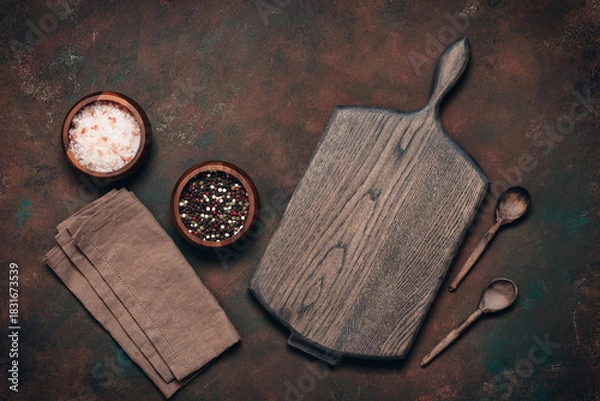 Fototapeta Culinary background with empty wooden board, wooden spoons, spices and linen napkin, dark grunge background, top view, flat lay, copy space