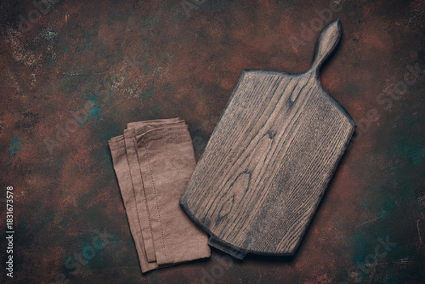 Fototapeta Empty wooden cutting board and linen napkin on dark rusty grunge background, culinary backdrop, top view, flat lay, copy space
