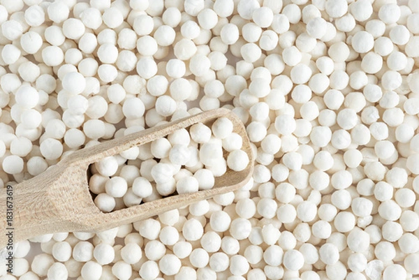 Fototapeta White dry tapioca pearls in wooden scoop on tapioca background. Top view of raw tapioca starch balls used for bubble tea or desserts. Tapioca pearls as healthy gluten free ingredient.