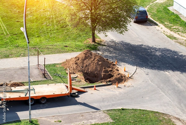 Fototapeta A dug hole in the city near the road. Concept of works on elimination of water channel leakage, laying pipes, repair works in the water supply system. Copy space for text