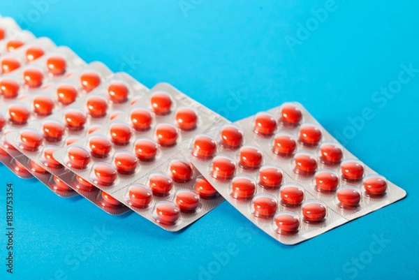 Fototapeta Blisters with red pills on a blue background. Concept of sedatives and tranquilizers in medicine, close-up