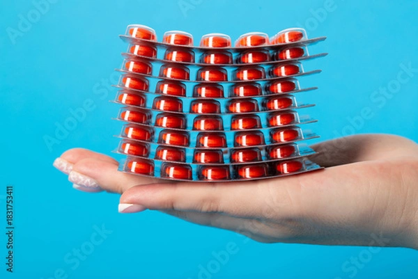 Fototapeta Stack of pills on the palm of the hand on a blue background, close-up. Concept of vitamins in pharmaceuticals, close-up