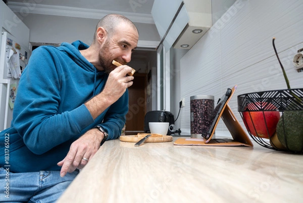 Obraz Man having toast for breakfast while using a tablet at home