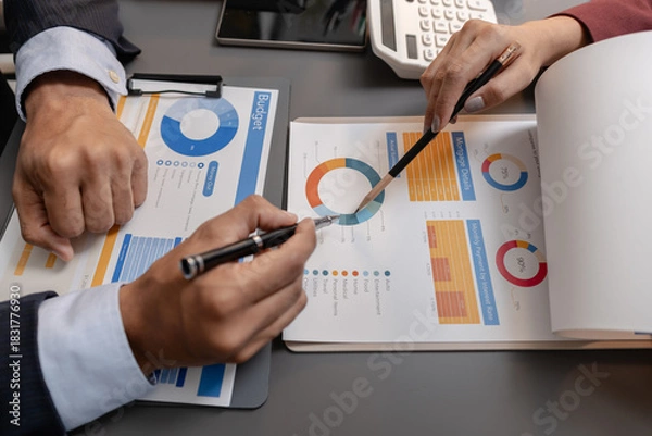 Fototapeta Business professionals reviewing financial charts and performance reports during a meeting, highlighting strategic planning, budget analysis, and teamwork in a modern corporate environment.