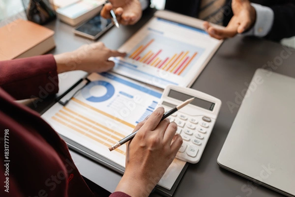 Fototapeta Business professionals meeting at a modern office table, reviewing charts and budget reports while discussing key financial insights and strategic plans for upcoming business decisions.