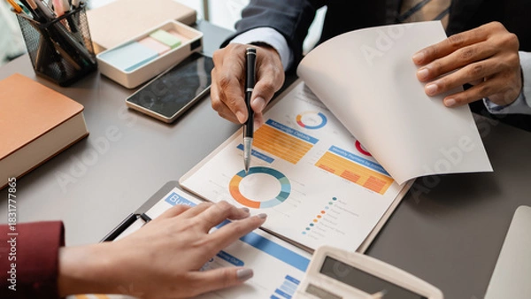 Obraz Business professionals meeting at a modern office table, reviewing charts and budget reports while discussing key financial insights and strategic plans for upcoming business decisions.