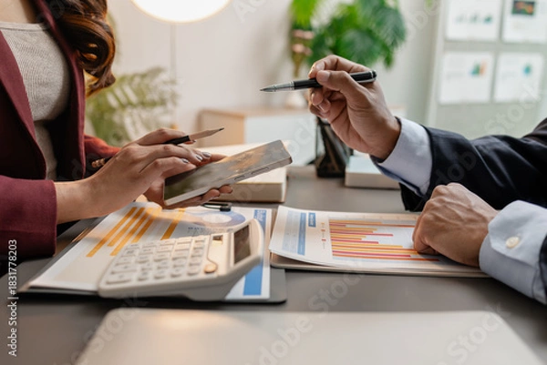 Fototapeta Business professionals meeting at a modern office table, reviewing charts and budget reports while discussing key financial insights and strategic plans for upcoming business decisions.