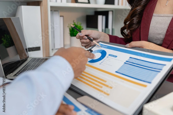 Fototapeta Business colleagues reviewing budget charts together in a modern office, focusing on financial insights, performance metrics, and strategic planning to support upcoming business decisions.