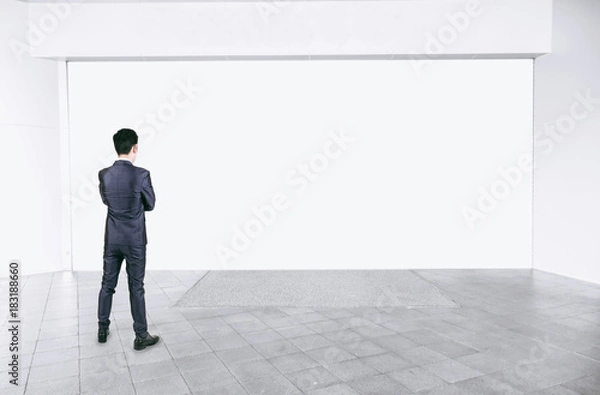 Fototapeta Businessman in black suit standing in empty interior with mock up white space