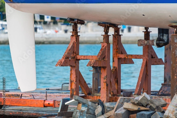 Fototapeta Boat hull maintenance with rusty stands in harbor setting