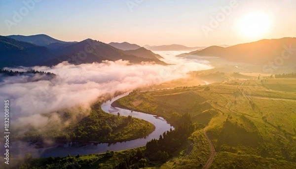 Fototapeta Aerial view of a river winding through a valley, surrounded by mountains and a layer of fog, illuminated by the warm light of sunrise.