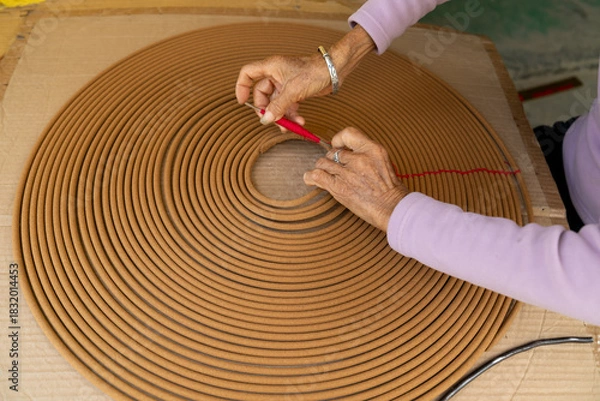 Fototapeta Artisan Hands Carefully Shaping Large Traditional Spiral Coil Incense with Red Thread Binding