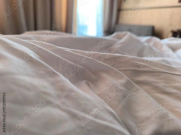 Fototapeta View of a wrinkled white blanket, unmade bed. concepts of comfortable sleep