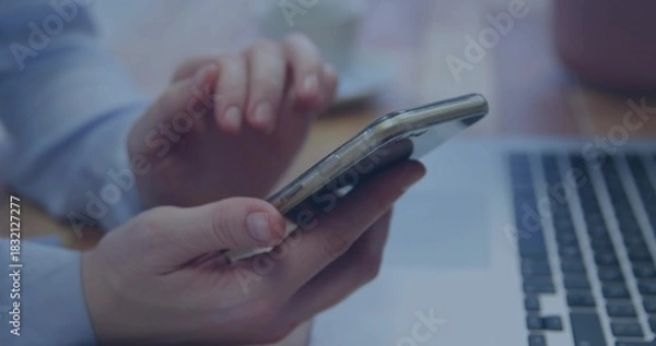 Obraz Tapping hands wearing light-blue cuff, holding smartphone at small home desk with laptop and mug