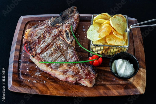 Fototapeta Grilled steak served on a wooden platter with crispy potato chips and fresh herbs, showcasing a delicious culinary presentation