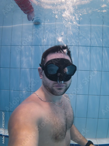 Fototapeta Underwater portrait of a male freediver wearing a black mask during a breath-holding and static apnea training session.