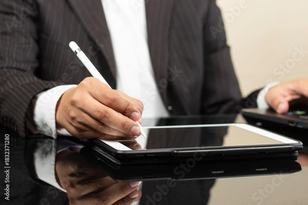 Fototapeta a business man on suit writing something on a tablet screen with a digital pen at the left side of the screen