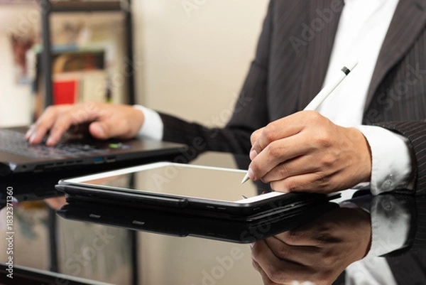 Fototapeta a CEO on suit writing something on a tablet with his left hand an a digital pen