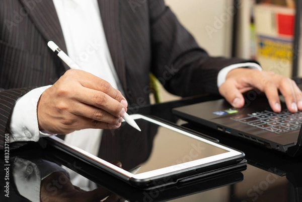 Fototapeta a CEO at the left side of the screen working with a digital pen over a tablet and a black laptop