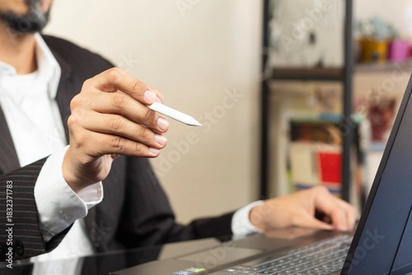 Fototapeta a CEO on suit working at home pointing with a white digital pen to something on the space at the left side of the screen