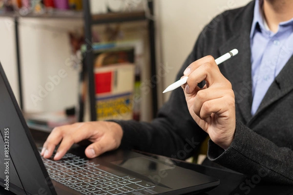 Fototapeta a modern business man pointing with his left hand with a white digital pen to a screen of a laptop