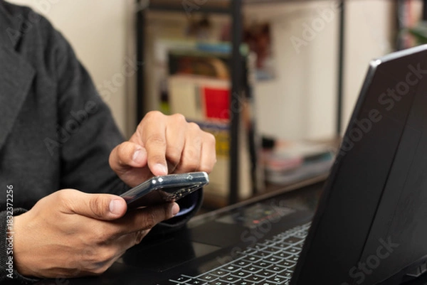 Fototapeta Close up to a modern business man pointing with his left index finger to a smartphone display over a laptop at the left side of the screen