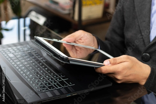 Fototapeta a modern business man holding a white tablet with his both hands in front of a laptop display