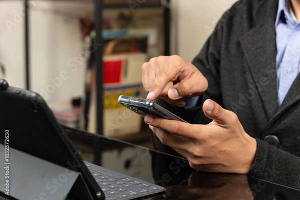 Fototapeta a modern CEO pointing with his index finger to the display of a smartphone in front of a tablet with keyboard