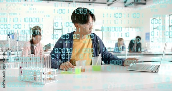 Obraz Mixing teen Asian student at school lab bench, with open laptop, goggles and binary overlay