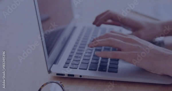 Fototapeta Typing woman's hands pressing keys on laptop keyboard at wooden desk, with eyeglasses nearby
