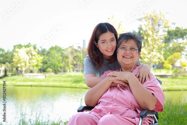Fototapeta Portrait of a caring daughter or caregiver, looking after an elderly patient sitting in a wheelchair to breathe fresh air outside. Elderly health care concept. copy space