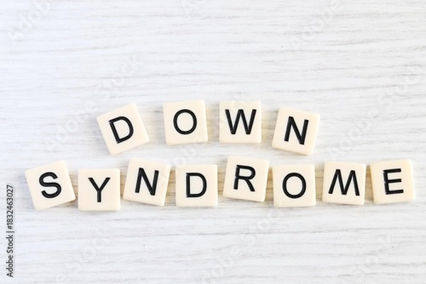 Fototapeta Close up shot of some plastic letter blocks spelling "Down Syndrome" in English on white wooden background.