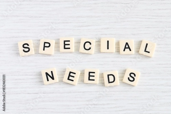Fototapeta Close up shot of some plastic letter blocks spelling "Special Needs" in English on white wooden background.