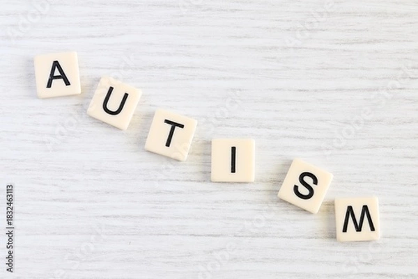 Fototapeta Close up shot of some plastic letter blocks spelling "Autism" in English on white wooden background.