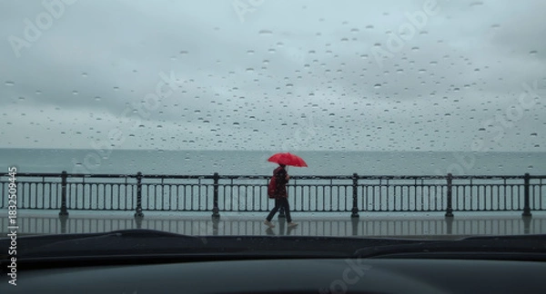 Fototapeta A person with a red umbrella walks alone through a rainy day creating a quiet and contemplative moment