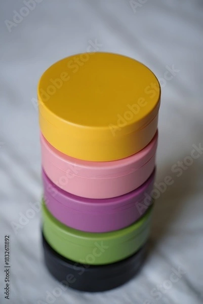 Fototapeta Stacked containers of various colors on a white surface creating a colorful tower